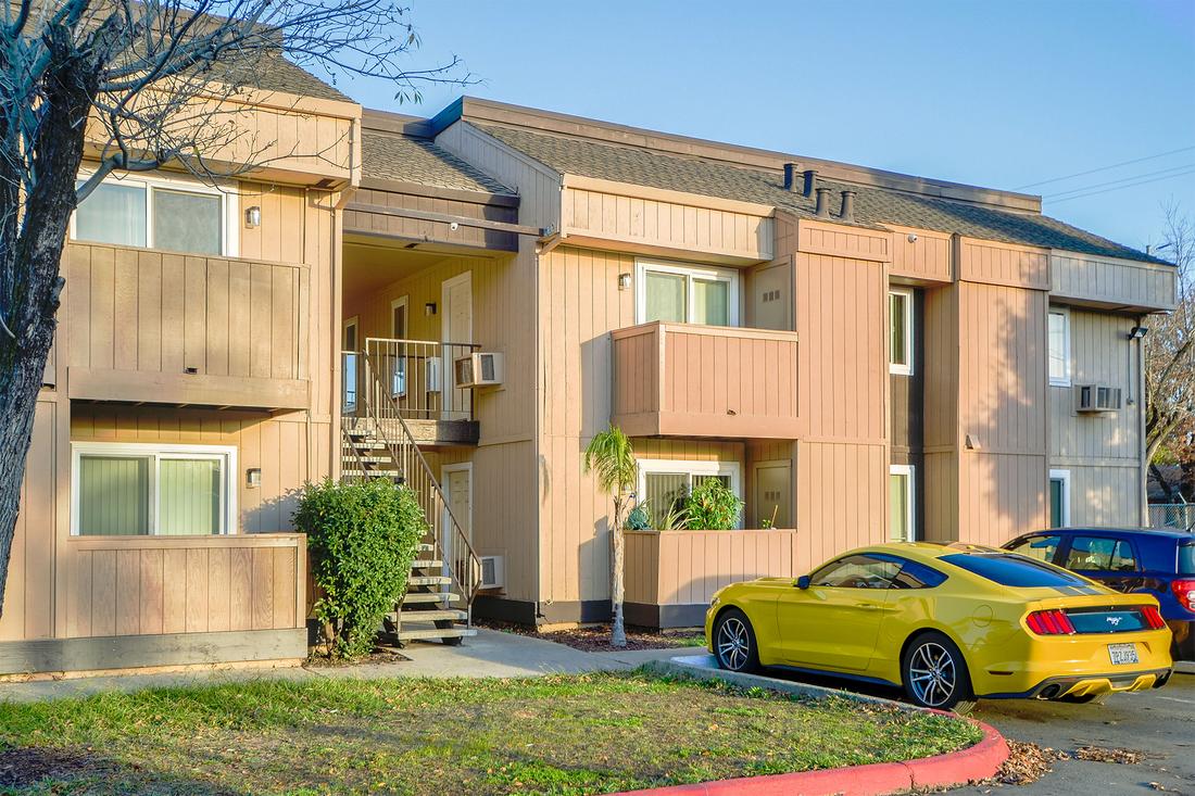 a yellow car parked in front of a two story apartment building.